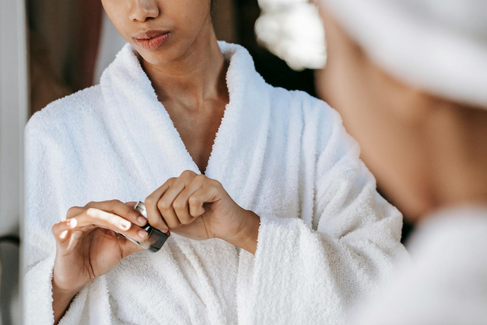 Young woman applying skincare cream in a bathrobe, reflecting self-care and wellness at home.