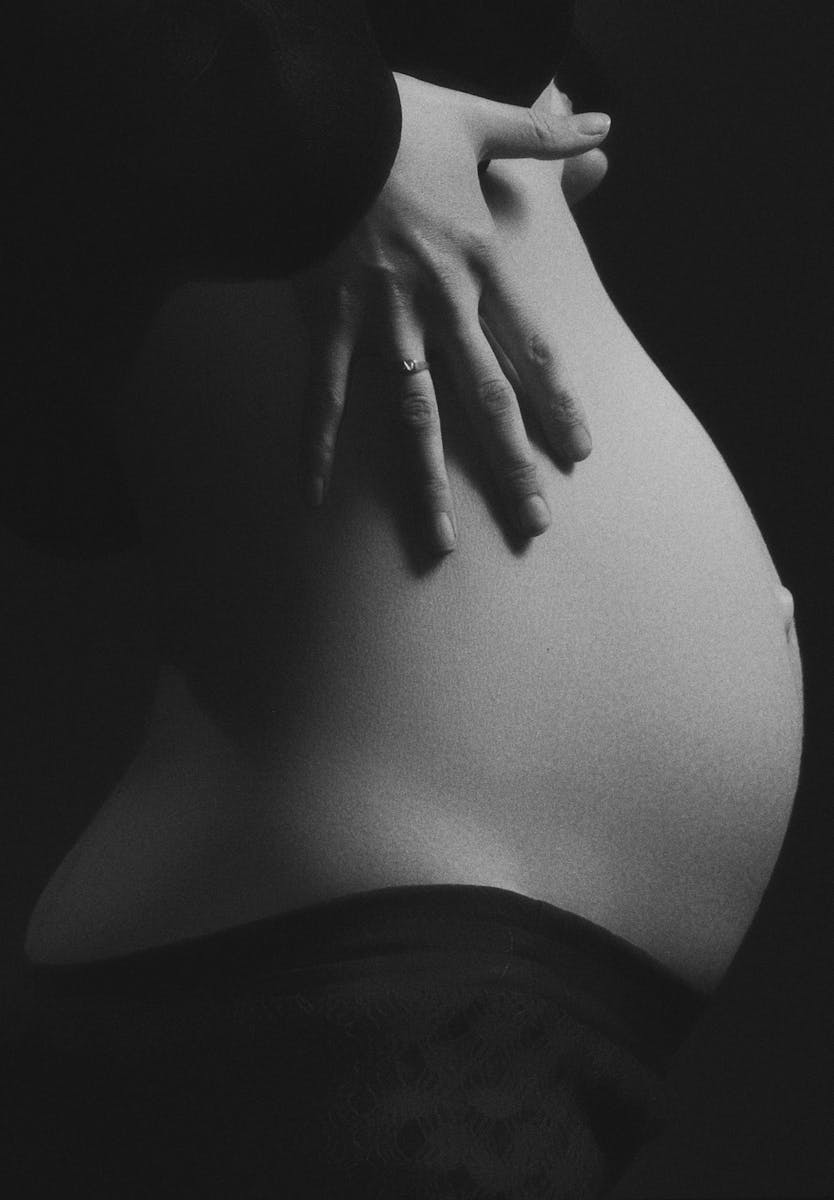 Intimate black and white photo of a pregnant woman's belly with hand gently resting.