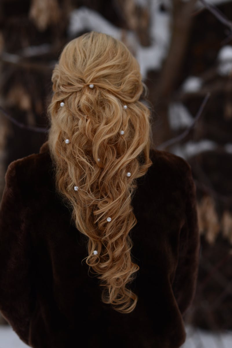 A woman with an intricate blonde hairstyle adorned with pearls, standing outdoors in winter.
